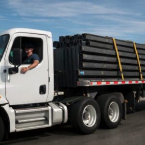 Owner operator driving flatbed truck hauling steel beams secured with straps, representing flatbed truck factoring for owner operators needing fast cash flow